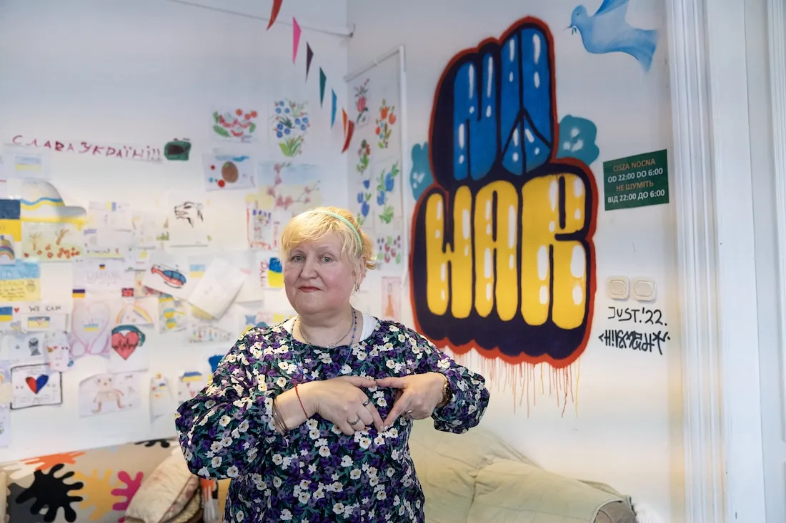elderly woman holds hands to heart with "No War" spraypainted behind her